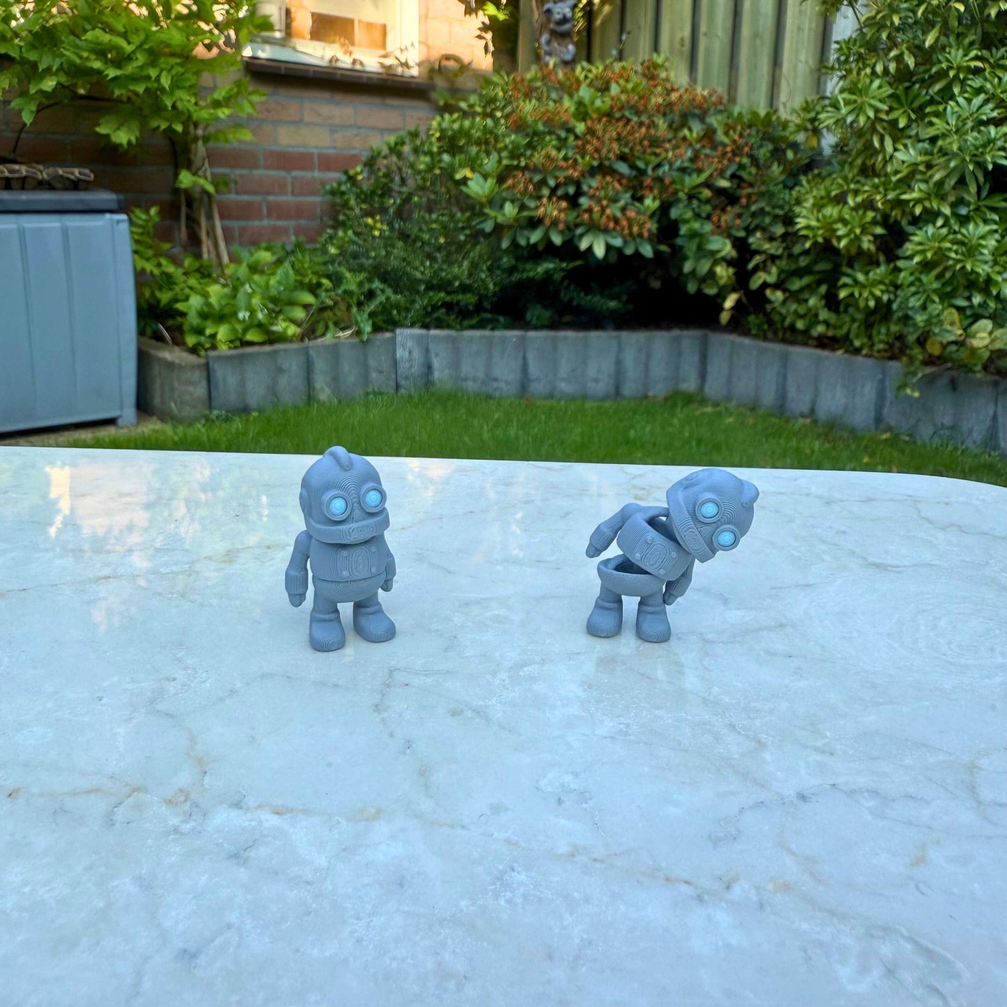 Twee 3D geprinte speelgoed robots met een vriendelijke, retro uitstraling.