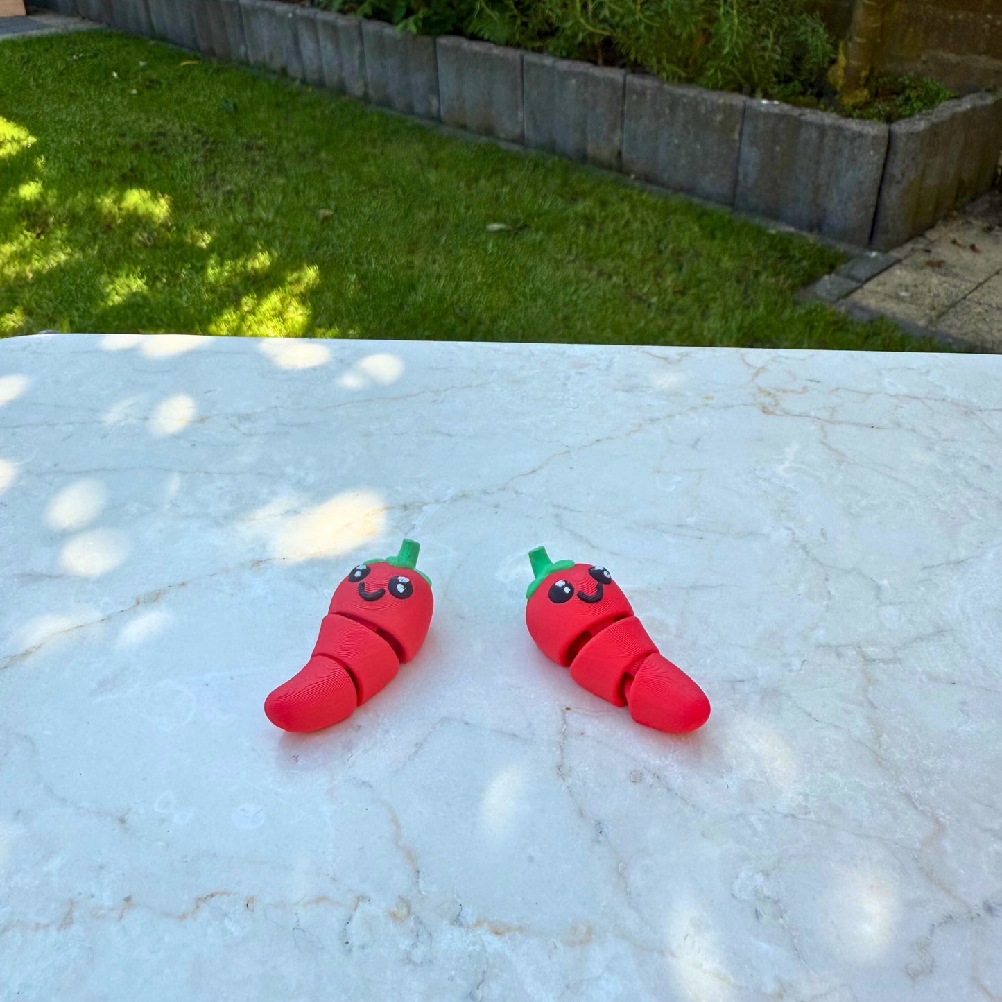 Detail van twee 3D geprinte speelgoed chilipepers, toont de articulatie en het schattige ontwerp.