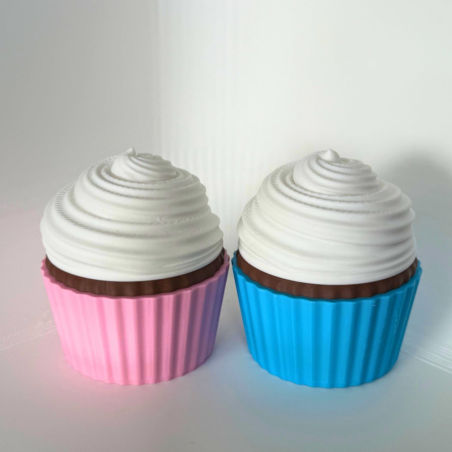 Twee schattige cupcake-opbergdoosjes in roze en blauw met witte glazuurdeksels, perfect voor kleine kindvriendelijke schatten