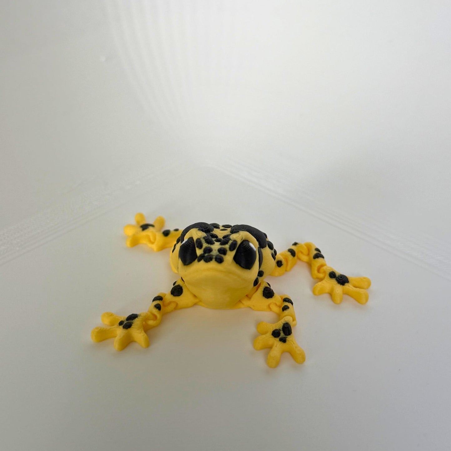 3D-geprinte gele gifkikker met zwarte vlekken – PLA speelgoedfiguur van een amazonepijlkikker, vooraanzicht
