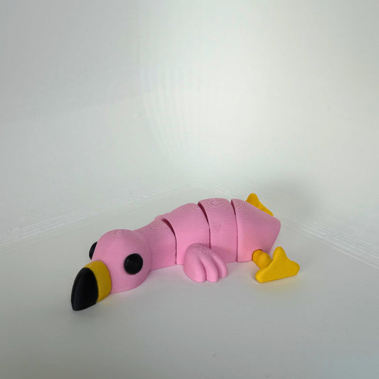 Lichtroze 3D-geprinte flamingo met gele poten en zwarte snavel, liggend op een witte ondergrond.