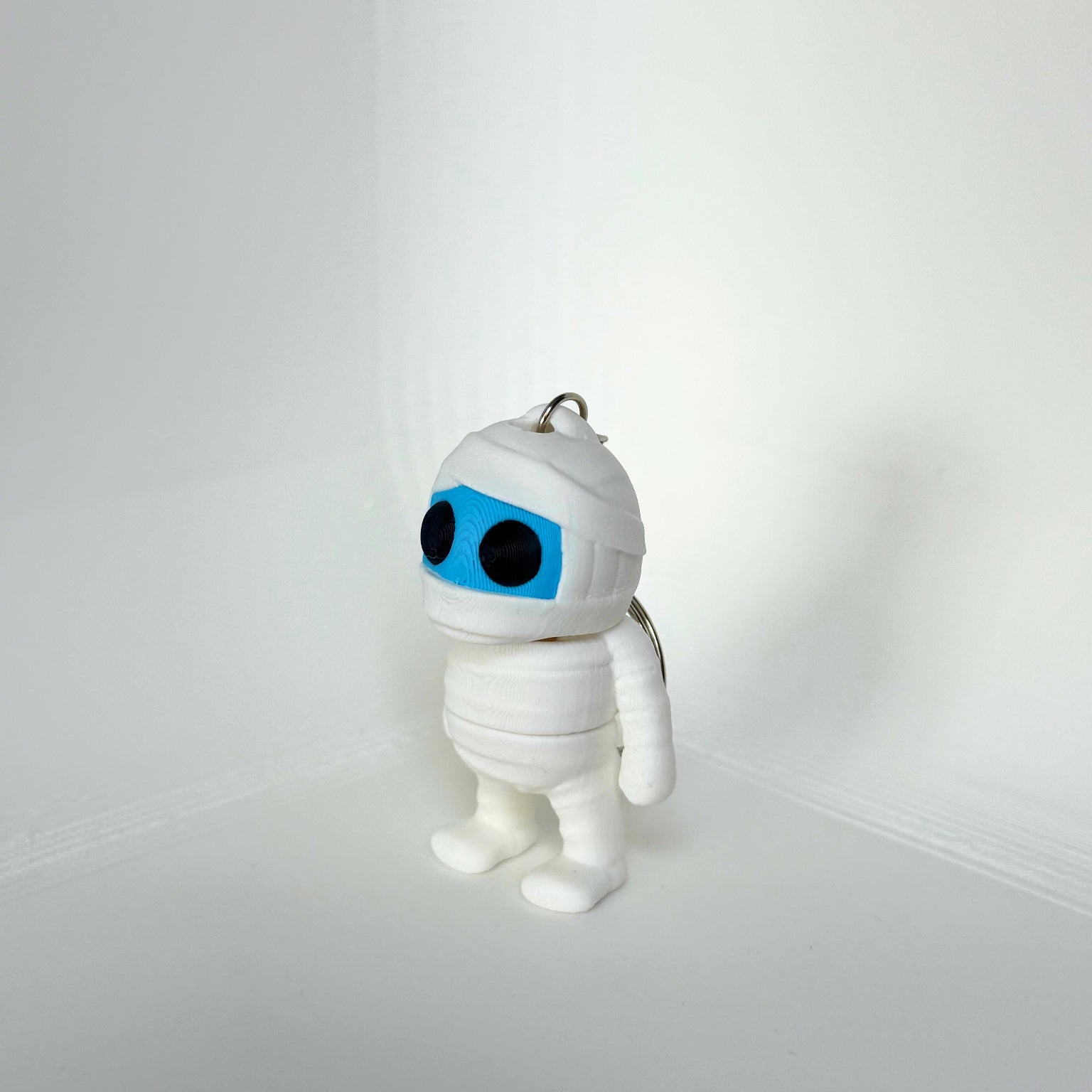 Kindvriendelijk speelgoed: wit 3D-geprint mummie figuurtje met blauwe gezicht en sleutelhanger, zijaanzicht