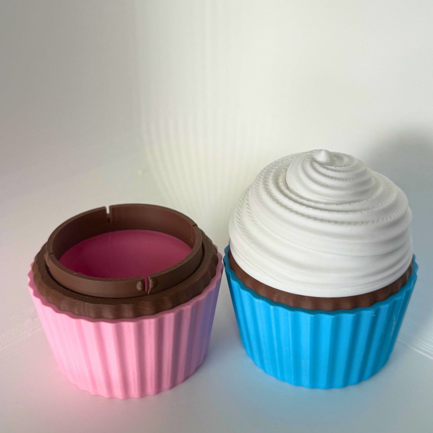 Roze cupcake-doosje geopend om de opbergruimte te tonen, naast een gesloten blauwe cupcake-container met wit glazuur