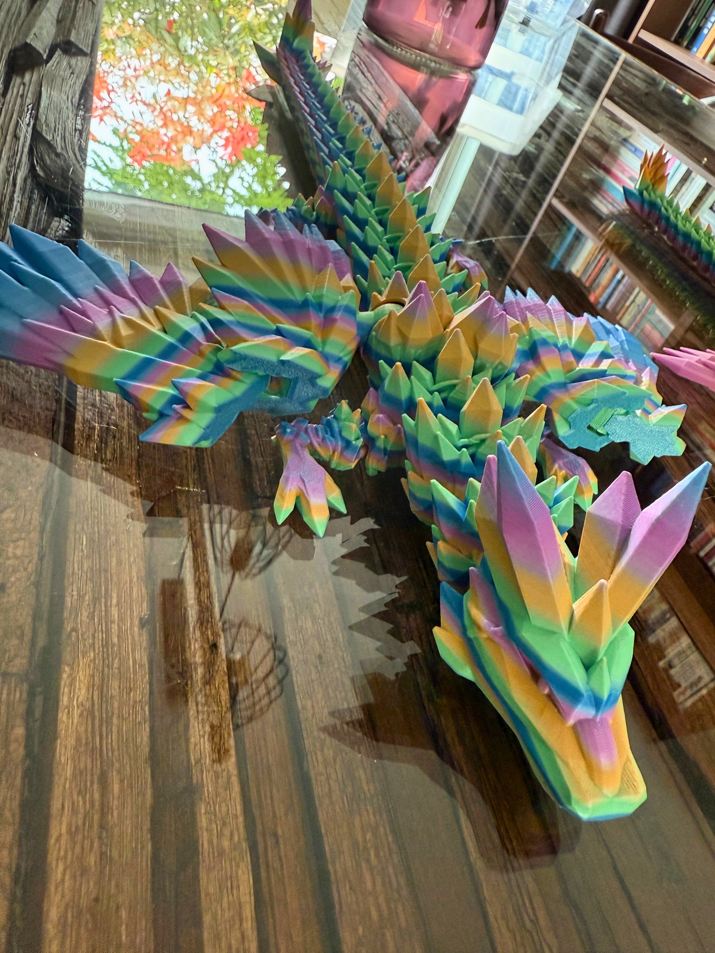 Close-up van het hoofd en de vleugels van een grote regenboogkleurige draak met reflecties op het tafelblad.