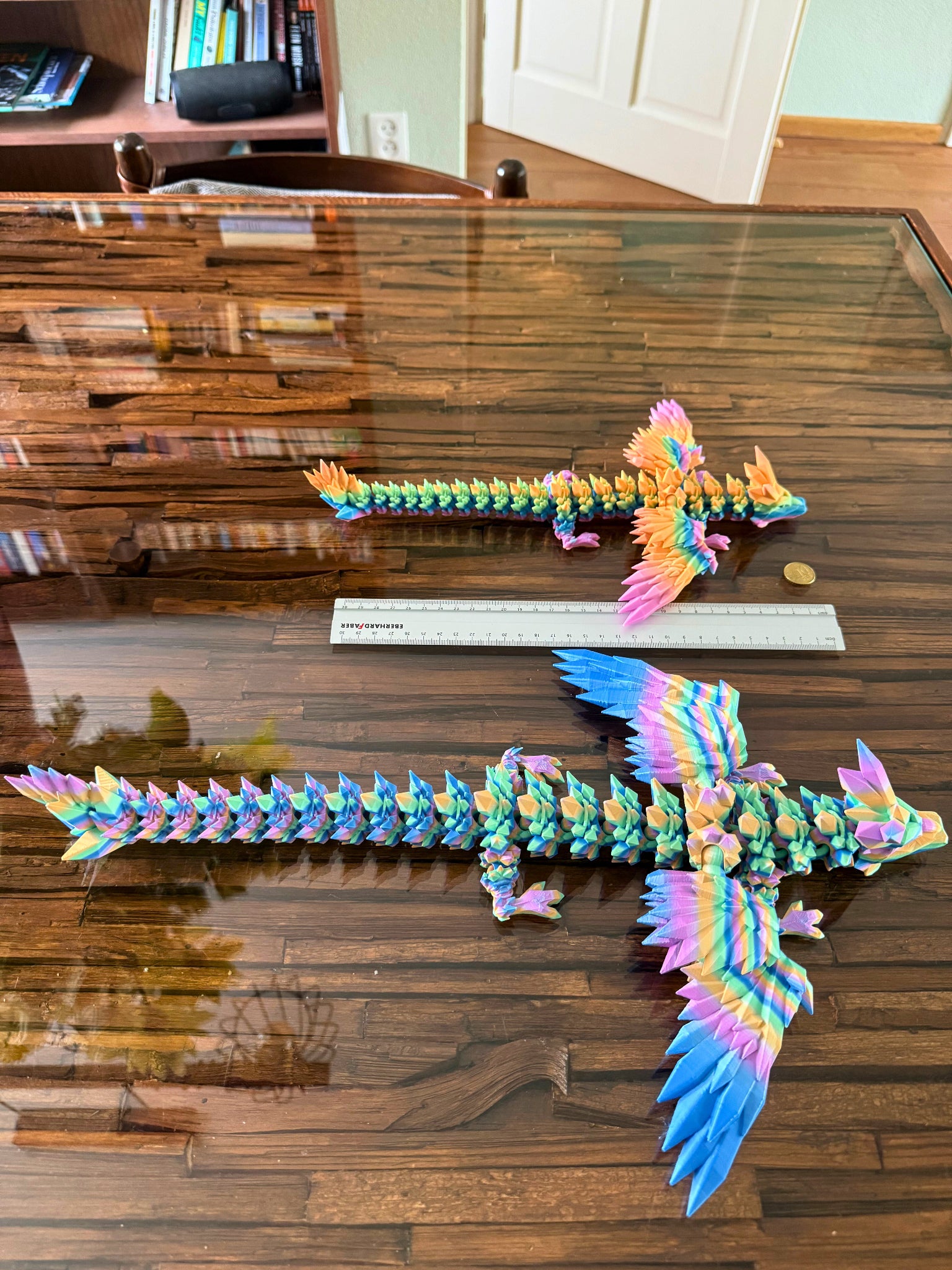 Twee articulerende regenboogdraken naast een liniaal en muntstuk voor schaalvergelijking.