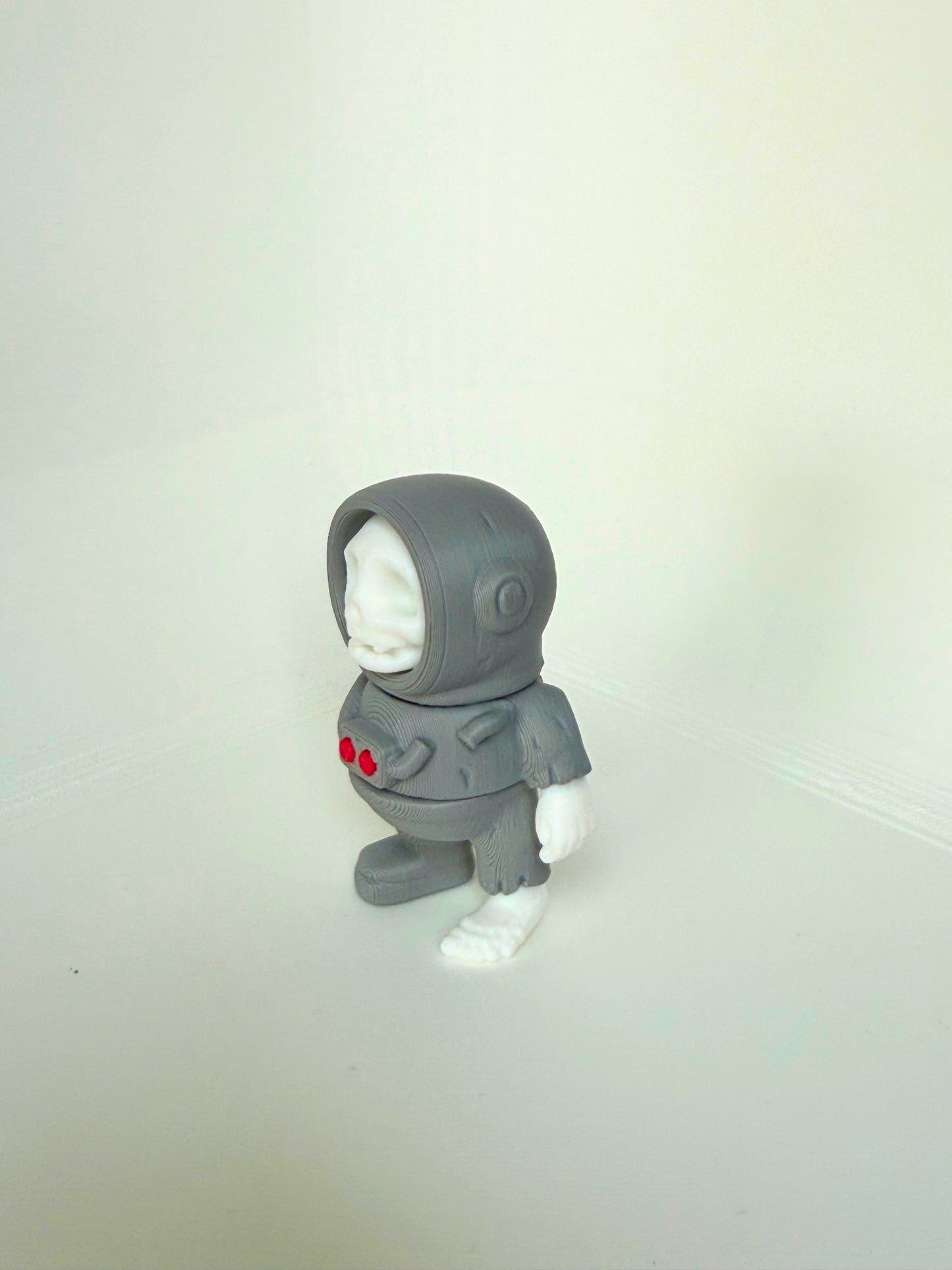 Grayscale 3D-printed skeleton astronaut figure with white skull and red buttons on the chest, shown from the front view.