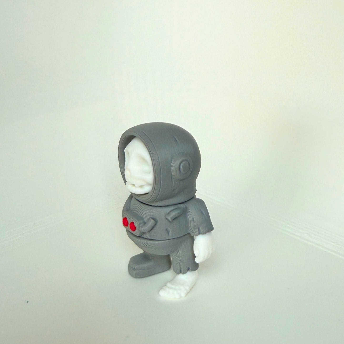 Grayscale 3D-printed skeleton astronaut figure with white skull and red buttons on the chest, shown from the front view.
