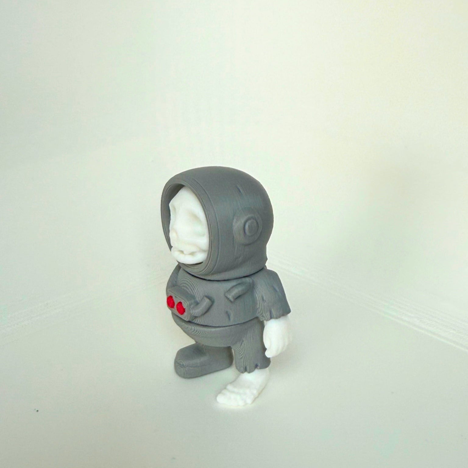 Grayscale 3D-printed skeleton astronaut figure with white skull and red buttons on the chest, shown from the front view.