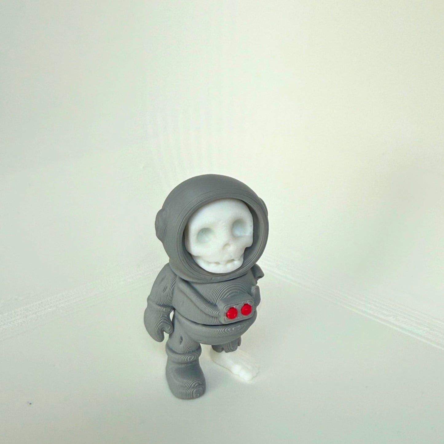 3D-printed dead astronaut toy seen from the side, featuring a skull face and detailed space suit with red chest lights.