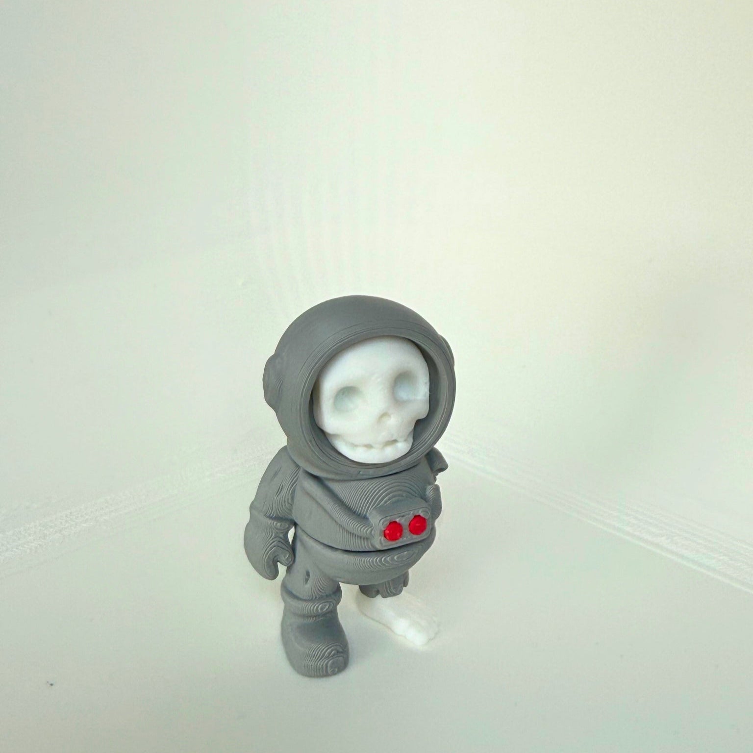 3D-printed dead astronaut toy seen from the side, featuring a skull face and detailed space suit with red chest lights.