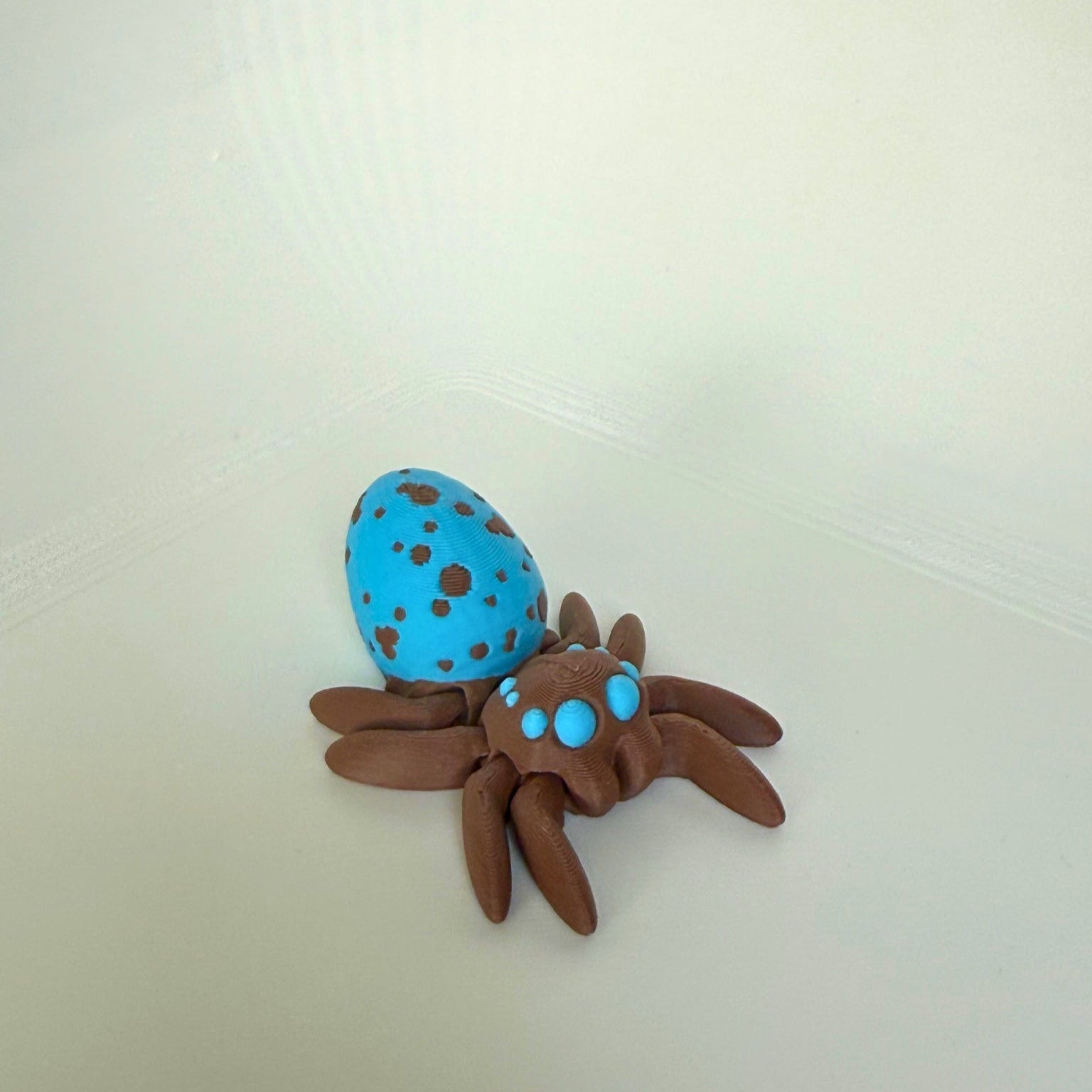 3D-printed brown spider toy with a shiny blue spotted body, shown from the front view on a white background.