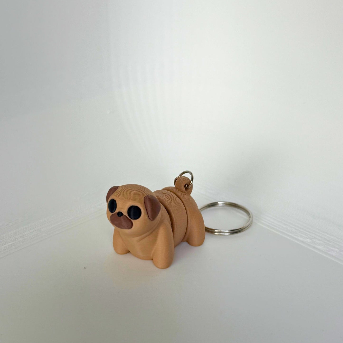 3D-geprinte mopshond sleutelhanger – schattig beige speelfiguur van PLA, liggend met zichtbare sleutelring