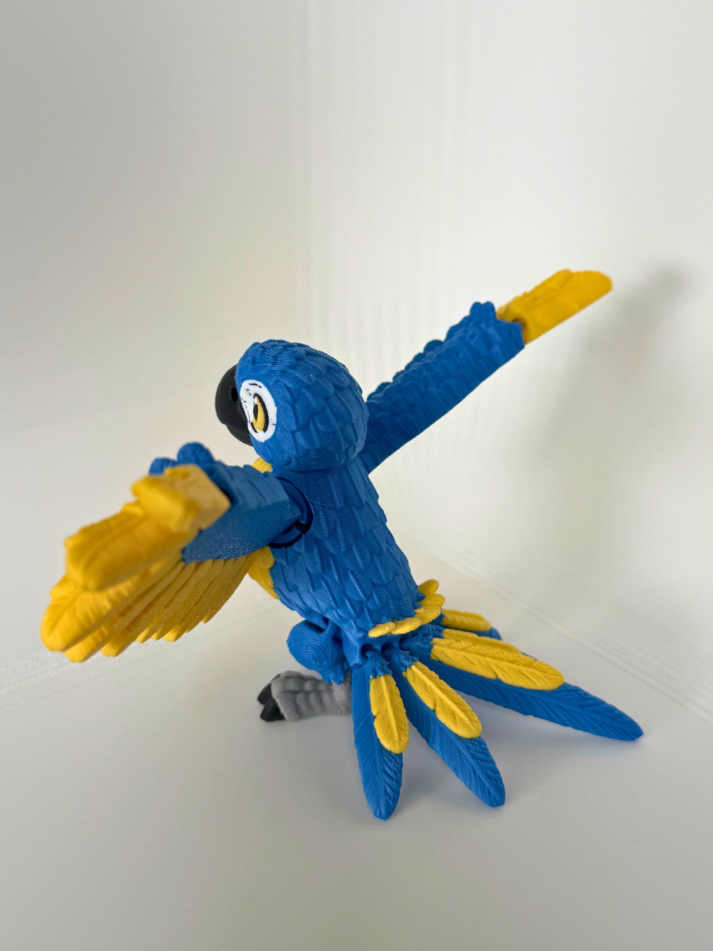 Zijkant van een kleurrijke blauwe papegaai met gele accenten, in een dynamische houding voor extra speelplezier.