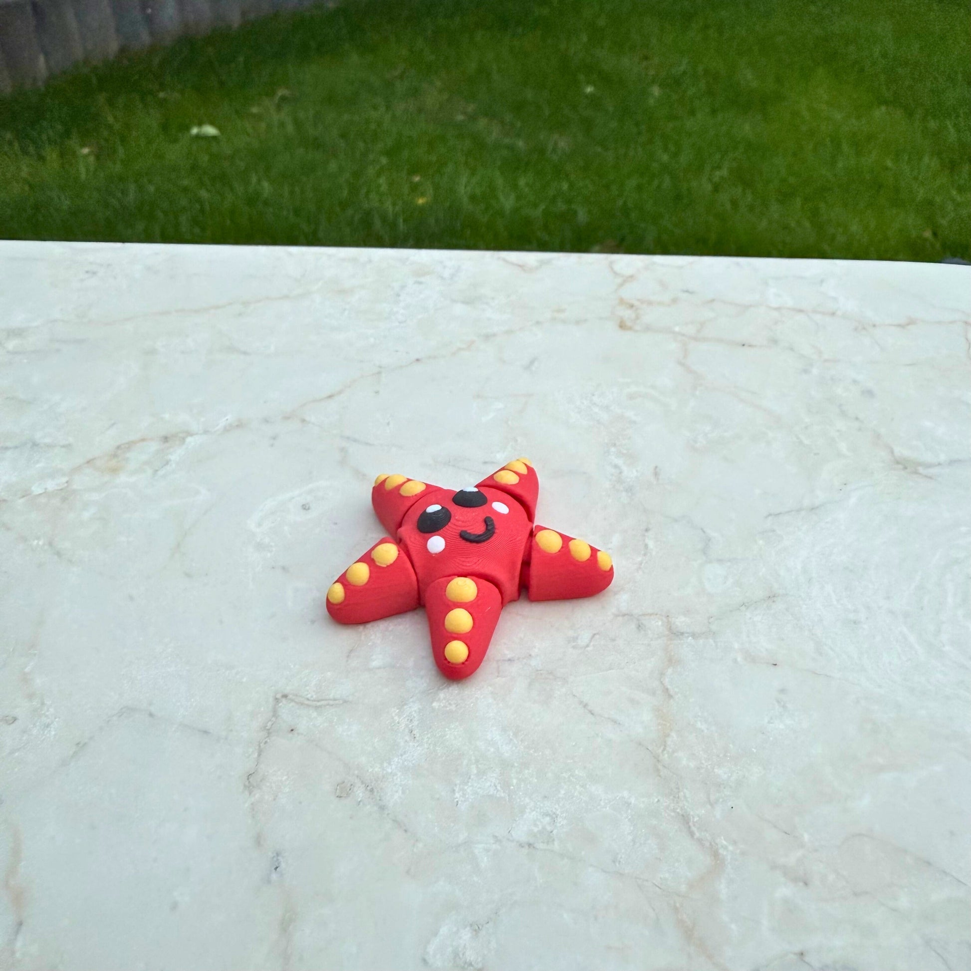 Rood met geel 3D geprint flexibel zeesterretje speelgoed, met beweegbare armen.