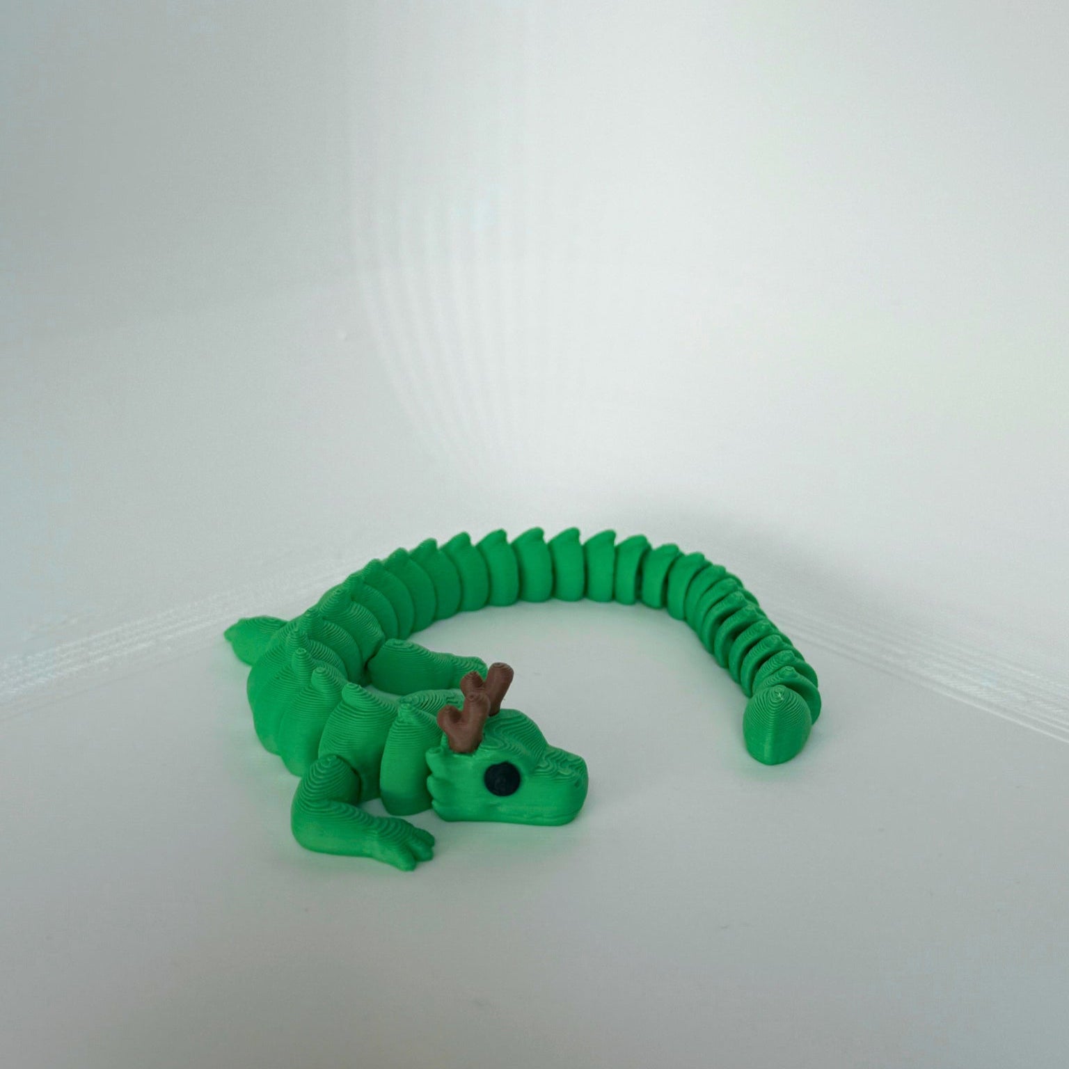 Speelse groene draak met bruine hoorns, volledig uitgestrekt op een witte achtergrond.