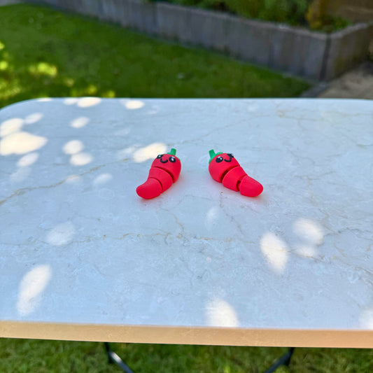Twee rode 3D geprinte flexibele chilipeper speelgoedfiguren, met beweegbare delen en een vrolijk gezicht.