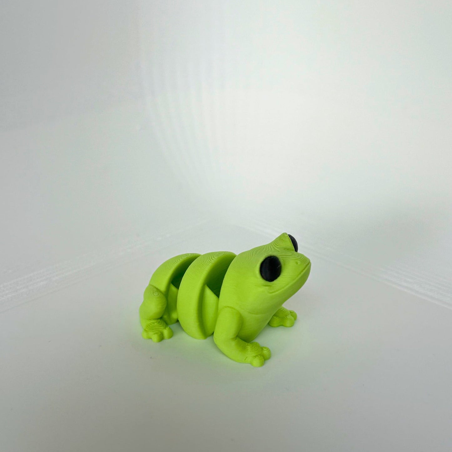 Groen 3D-geprint kikker speelfiguur met grote zwarte ogen, zittend op een witte achtergrond