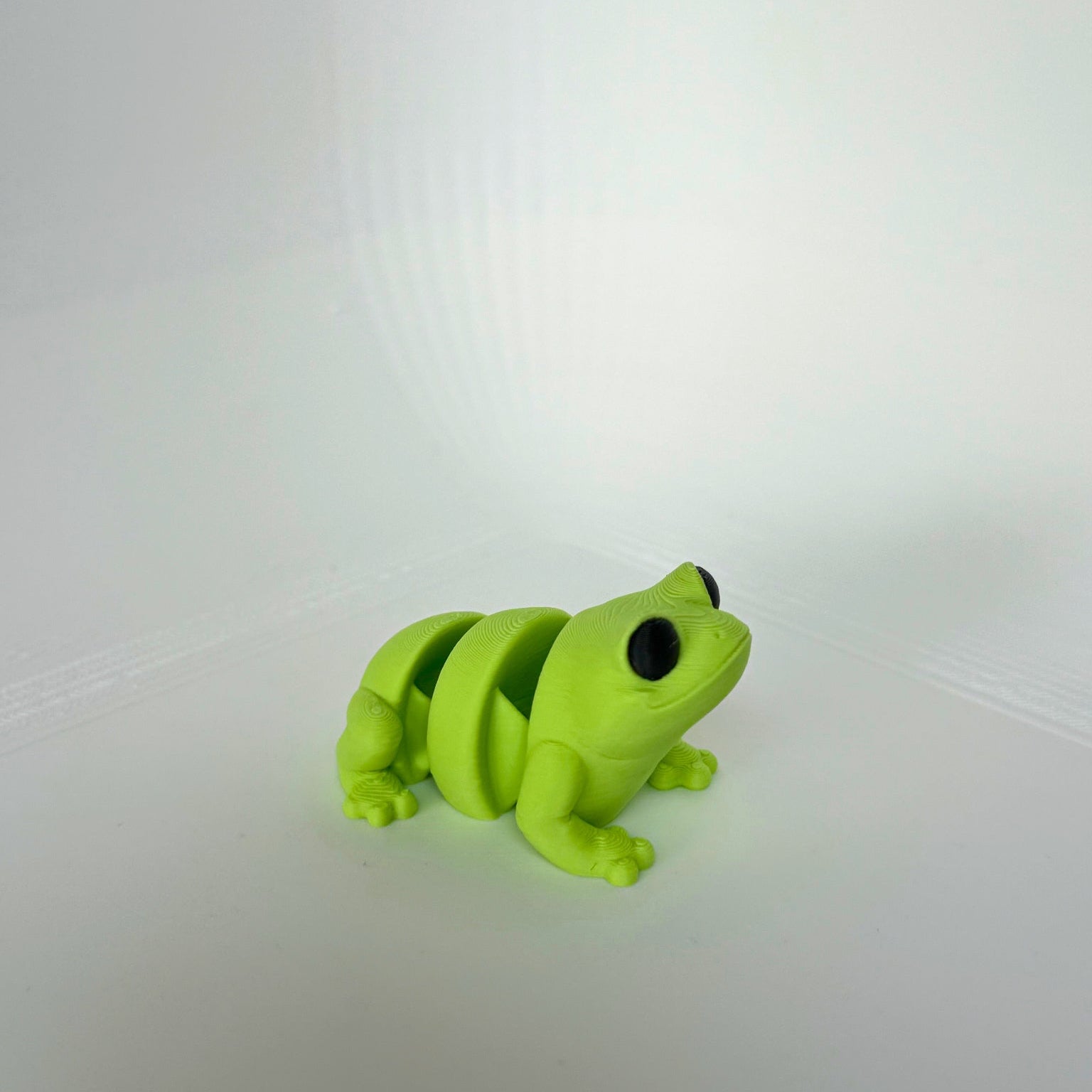Groen 3D-geprint kikker speelfiguur met grote zwarte ogen, zittend op een witte achtergrond