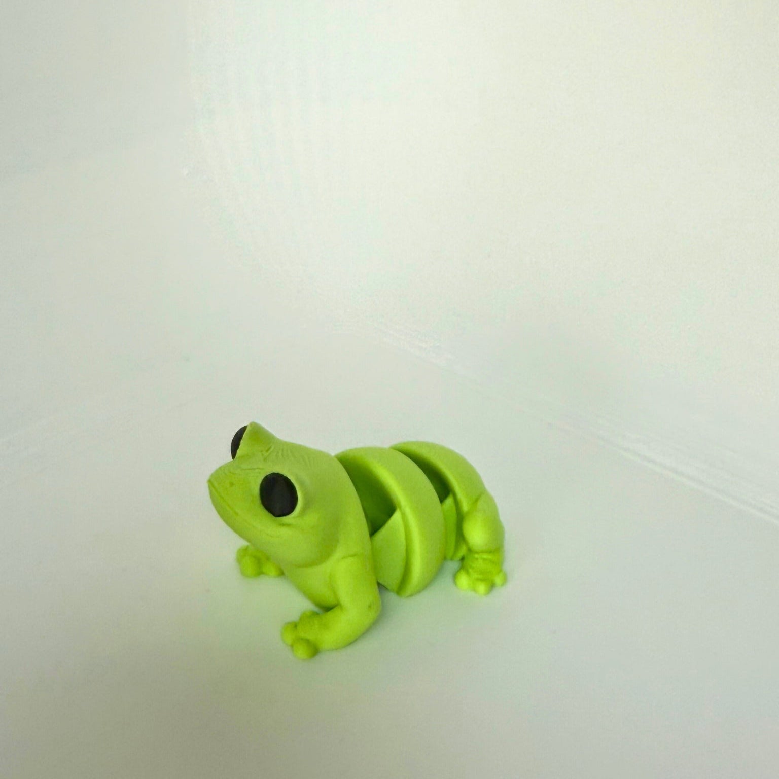 Lichtgroene kikker speelgoedfiguur van PLA met scharnierende delen, van schuin achteren gefotografeerd