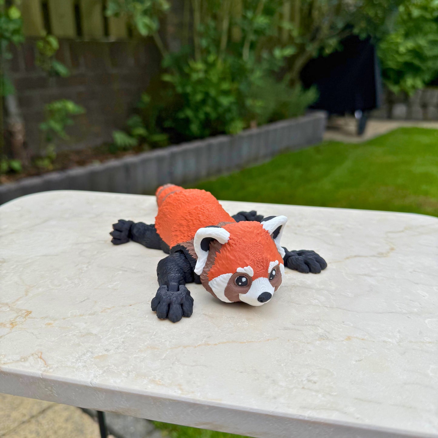 Zijaanzicht van een flexibel model van een 3D geprinte rode panda, speelgoed met beweegbare delen.