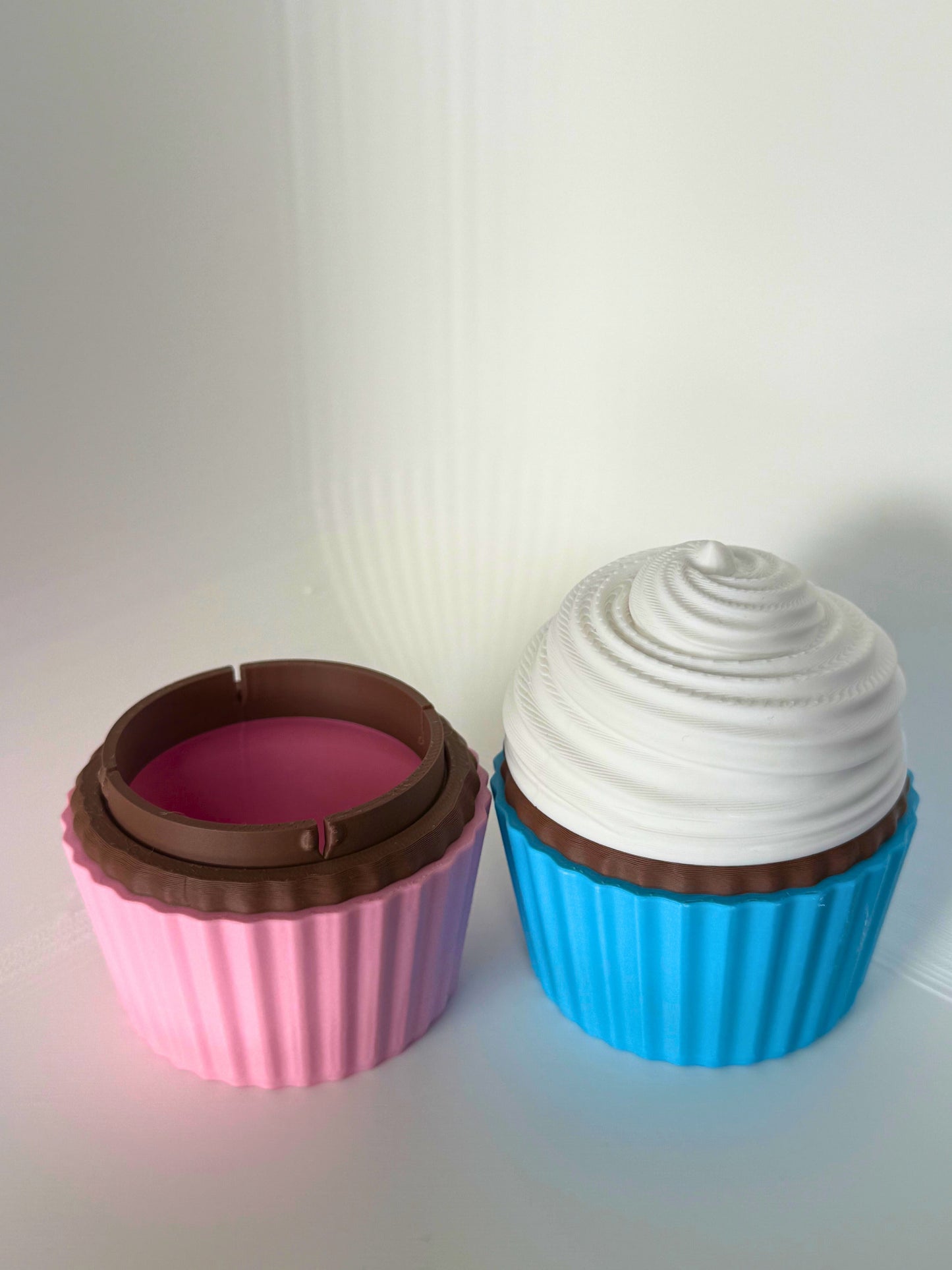 Roze cupcake-doosje geopend om de opbergruimte te tonen, naast een gesloten blauwe cupcake-container met wit glazuur
