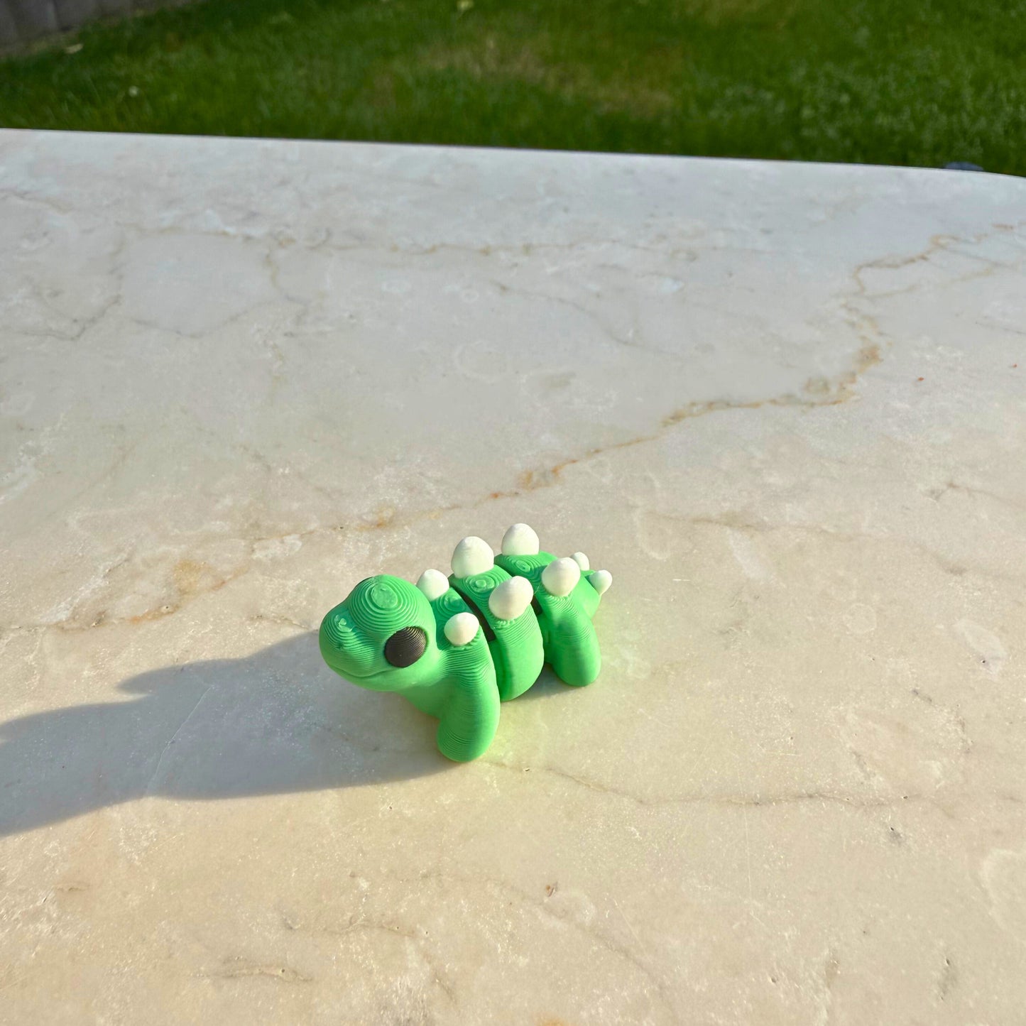 Schattig 3D geprint speelgoed baby stegosaurus, toont de articulatie en details.